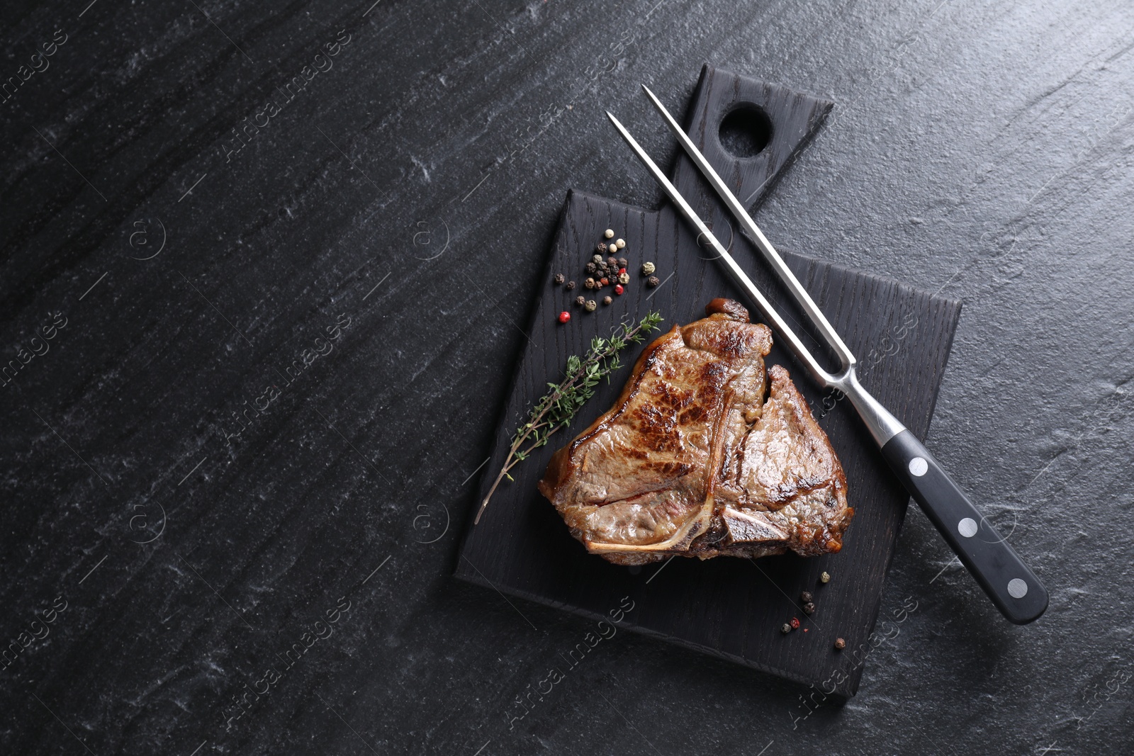 Photo of Delicious fried beef meat, thyme, peppercorns and fork on black table, top view. Space for text