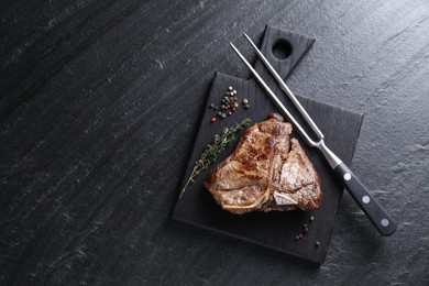 Photo of Delicious fried beef meat, thyme, peppercorns and fork on black table, top view. Space for text