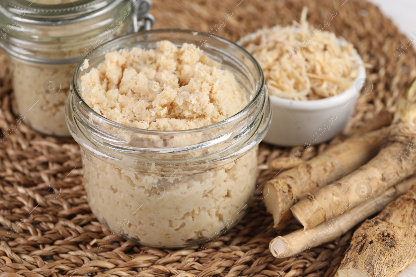 Photo of Tasty prepared horseradish and roots on wicker mat, closeup