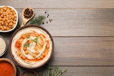 Photo of Delicious hummus with chickpeas and different ingredients on wooden table, flat lay. Space for text