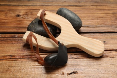 Photo of Slingshot with stones on wooden table, closeup