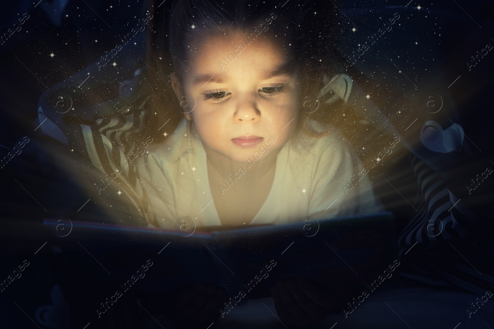 Image of Cute little child reading magic book in darkness