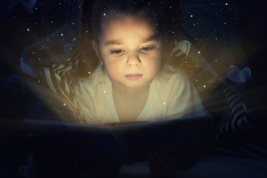 Cute little child reading magic book in darkness
