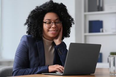 Photo of Young woman working on laptop at table in office