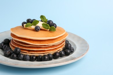 Stack of tasty pancakes with blueberries, butter and mint on light blue background, closeup. Space for text