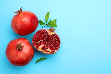 Photo of Fresh pomegranates and green leaves on light blue background, flat lay. Space for text