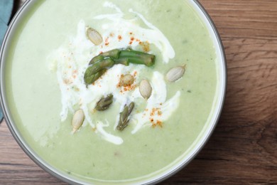 Delicious asparagus soup with pumpkin seeds on wooden table, top view