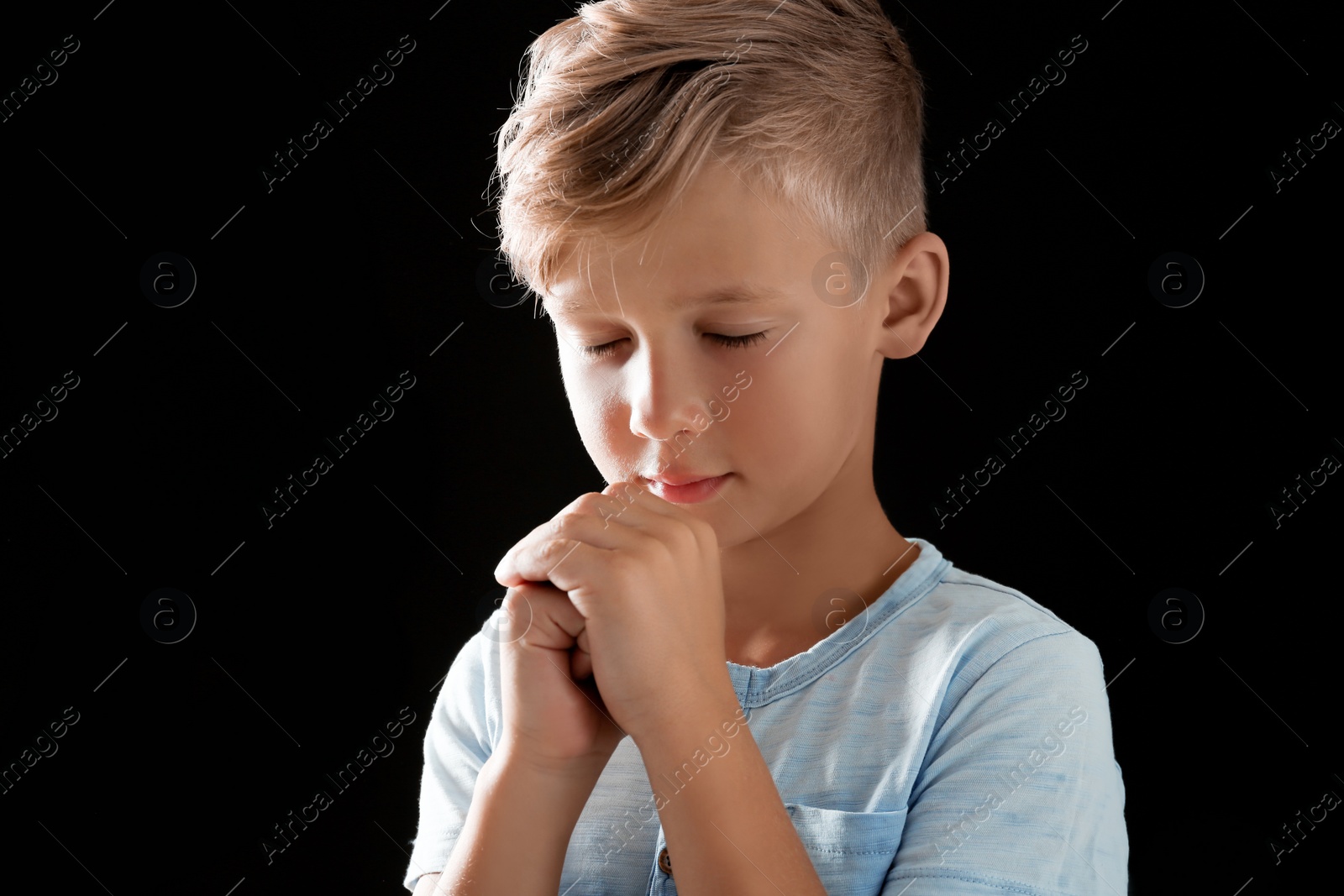 Photo of Little boy with hands clasped together for prayer on black background