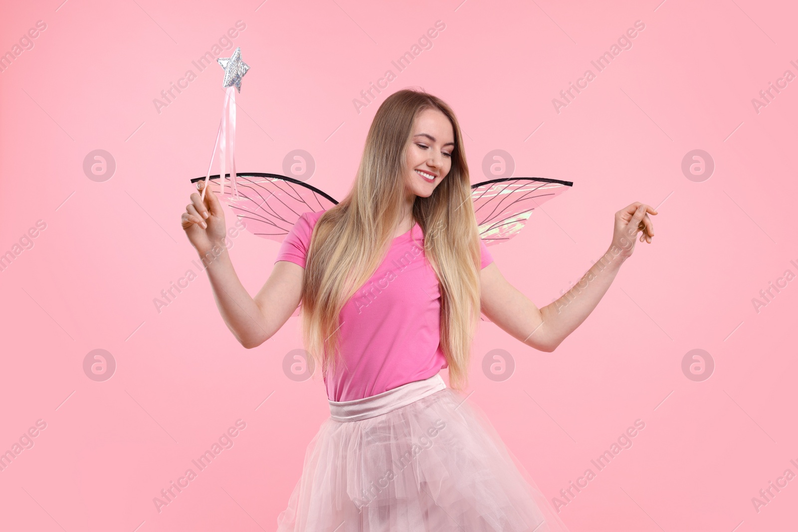 Photo of Beautiful girl in fairy costume with wings and magic wand on pink background