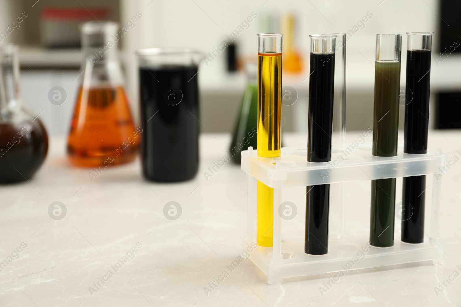 Photo of Laboratory glassware with different types of crude oil on light marble table, space for text