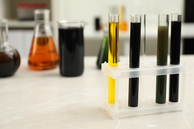Laboratory glassware with different types of crude oil on light marble table, space for text