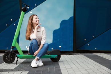 Photo of Happy woman sitting on modern electric kick scooter on city street, space for text