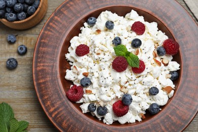 Photo of Fresh cottage cheese with berries and mint in plate on wooden table, flat lay