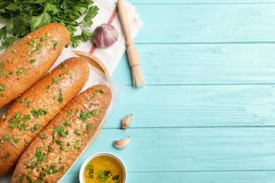 Photo of Loaves of delicious bread with garlic and herbs on light blue wooden table, flat lay. Space for text