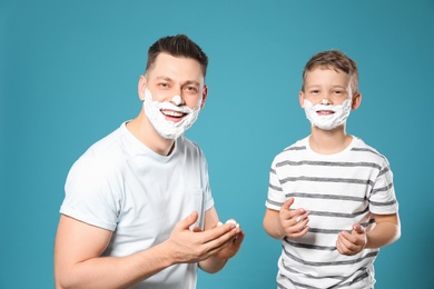 Photo of Happy dad and son with shaving foam on faces against blue background