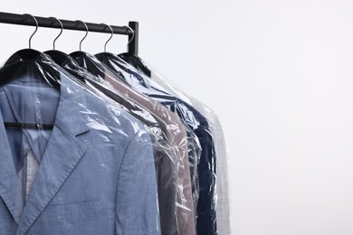 Dry-cleaning service. Many different clothes in plastic bags hanging on rack against white background, space for text