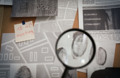 Looking through magnifying glass at fingerprints on detective board, closeup
