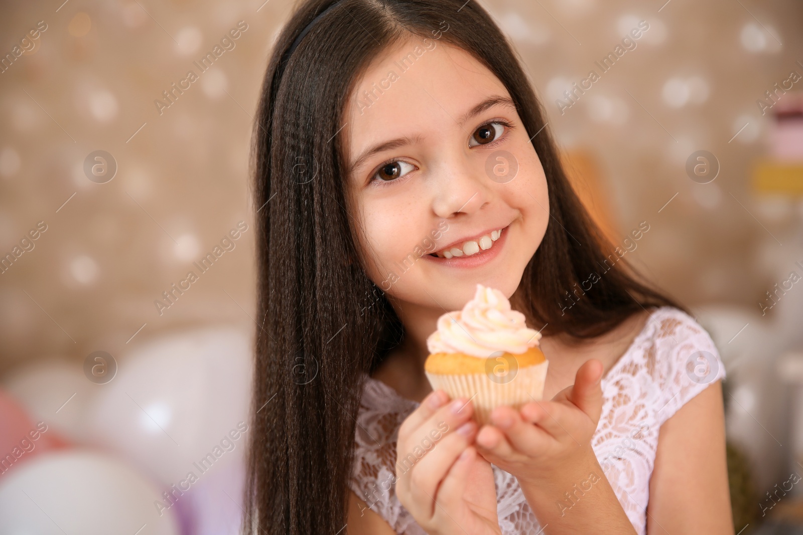 Photo of Happy little girl with birthday cupcake in beautifully decorated room at home