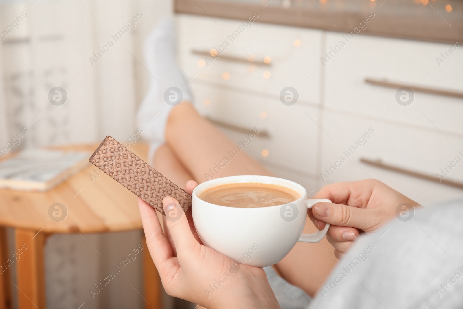 Photo of Woman having delicious wafer and coffee for breakfast indoors, closeup