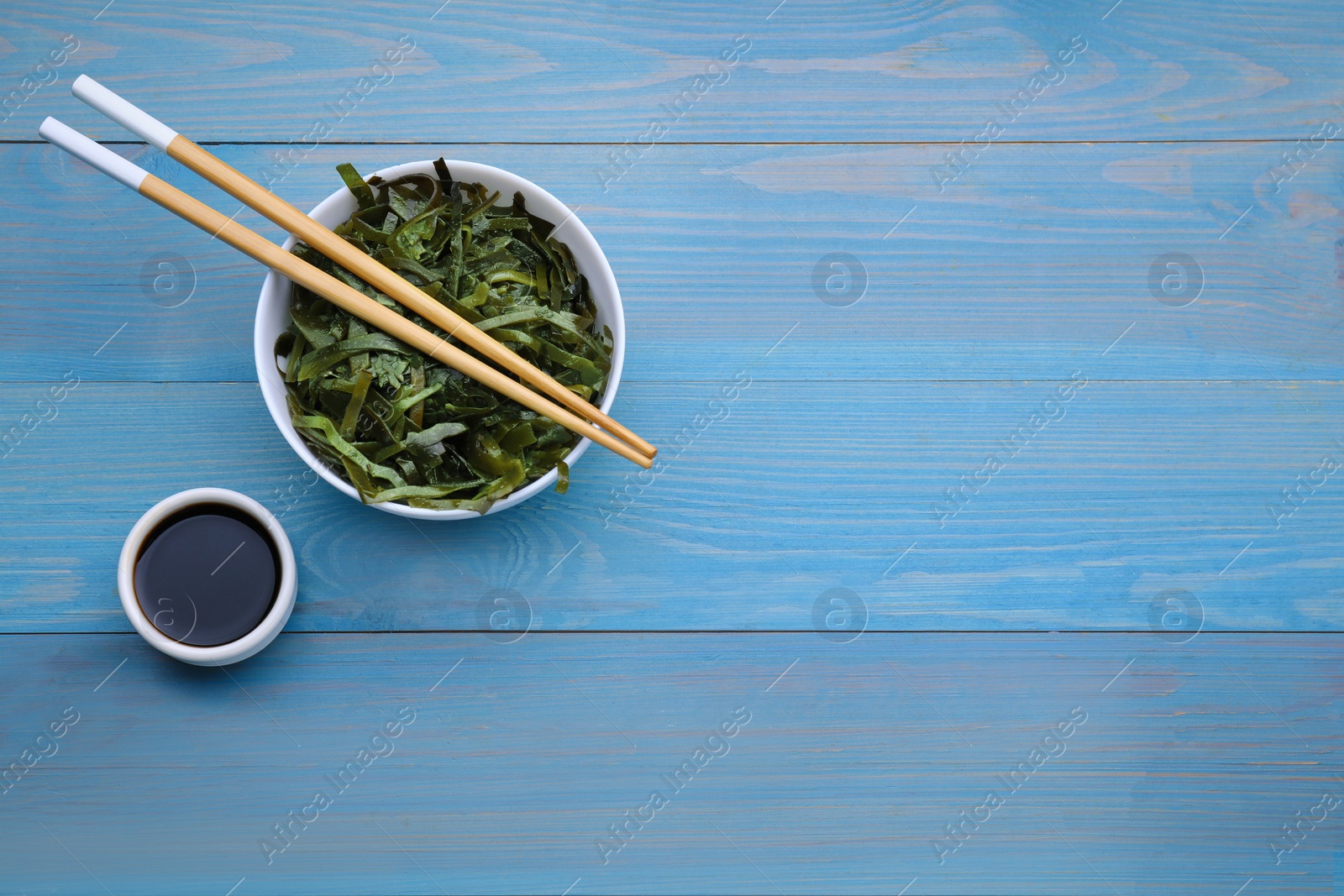 Photo of Fresh laminaria (kelp) seaweed served on light blue wooden table, flat lay. Space for text