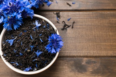 Bowl with dry tea leaves and cornflowers on wooden table, flat lay. Space for text