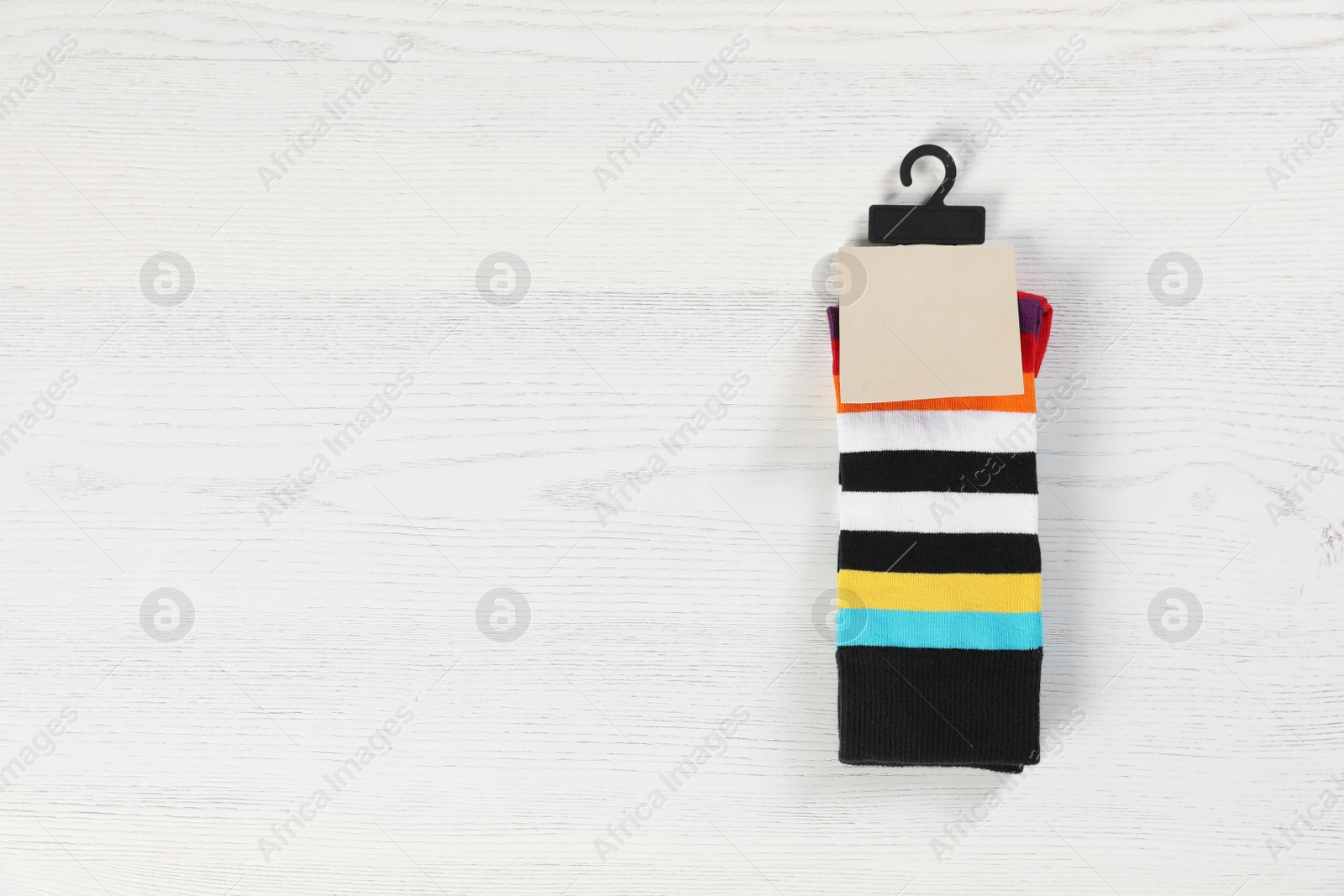 Photo of Pair of socks with tag and space for design on light wooden background