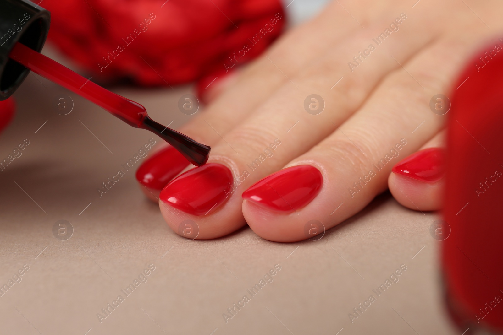 Photo of Woman painting nails with red polish on beige background, closeup