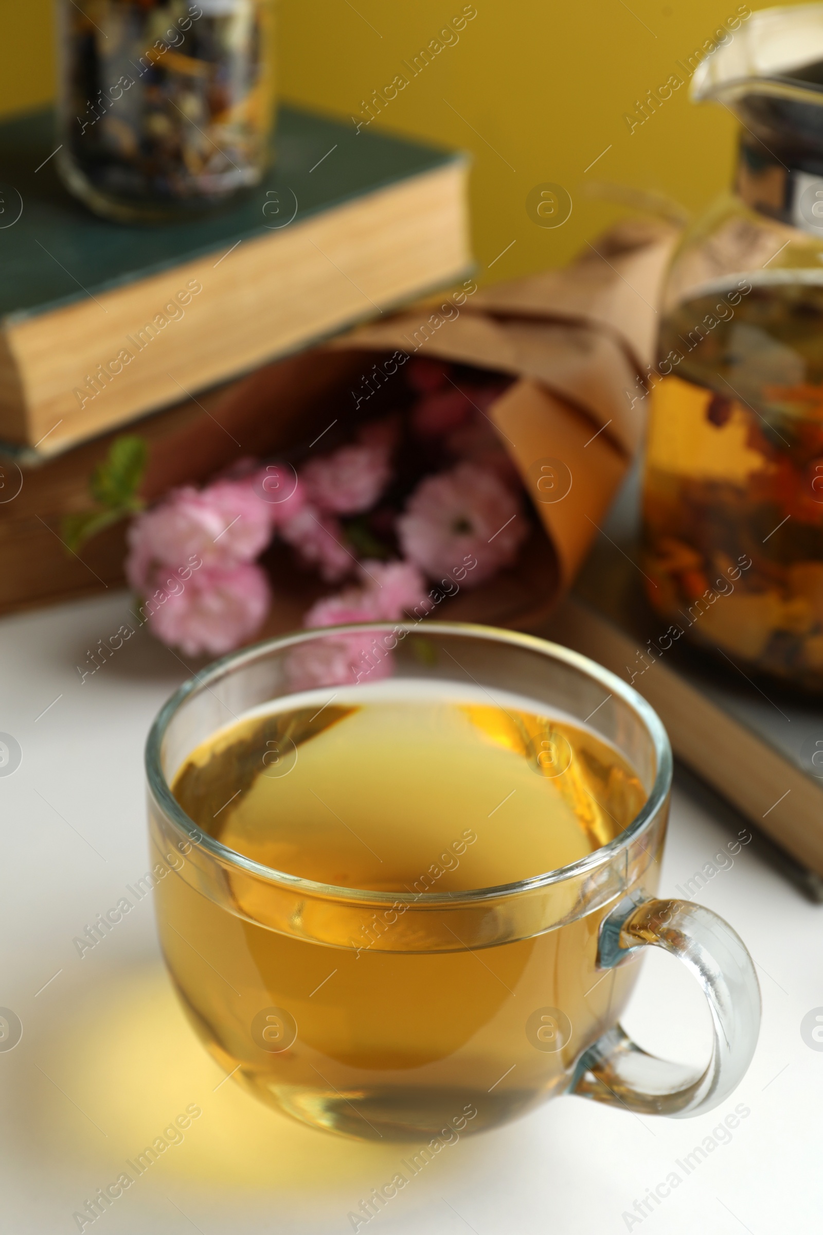 Photo of Glass cup of freshly brewed tea and flowers on light table