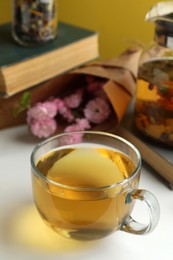 Photo of Glass cup of freshly brewed tea and flowers on light table