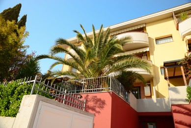 Beautiful apartment building with tropical trees in yard on sunny day, low angle view