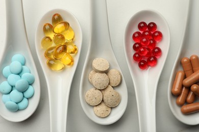 Photo of Spoons with different dietary supplements on white table, flat lay