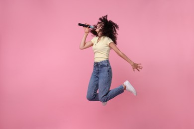 Photo of Beautiful young woman with microphone singing and jumping on pink background