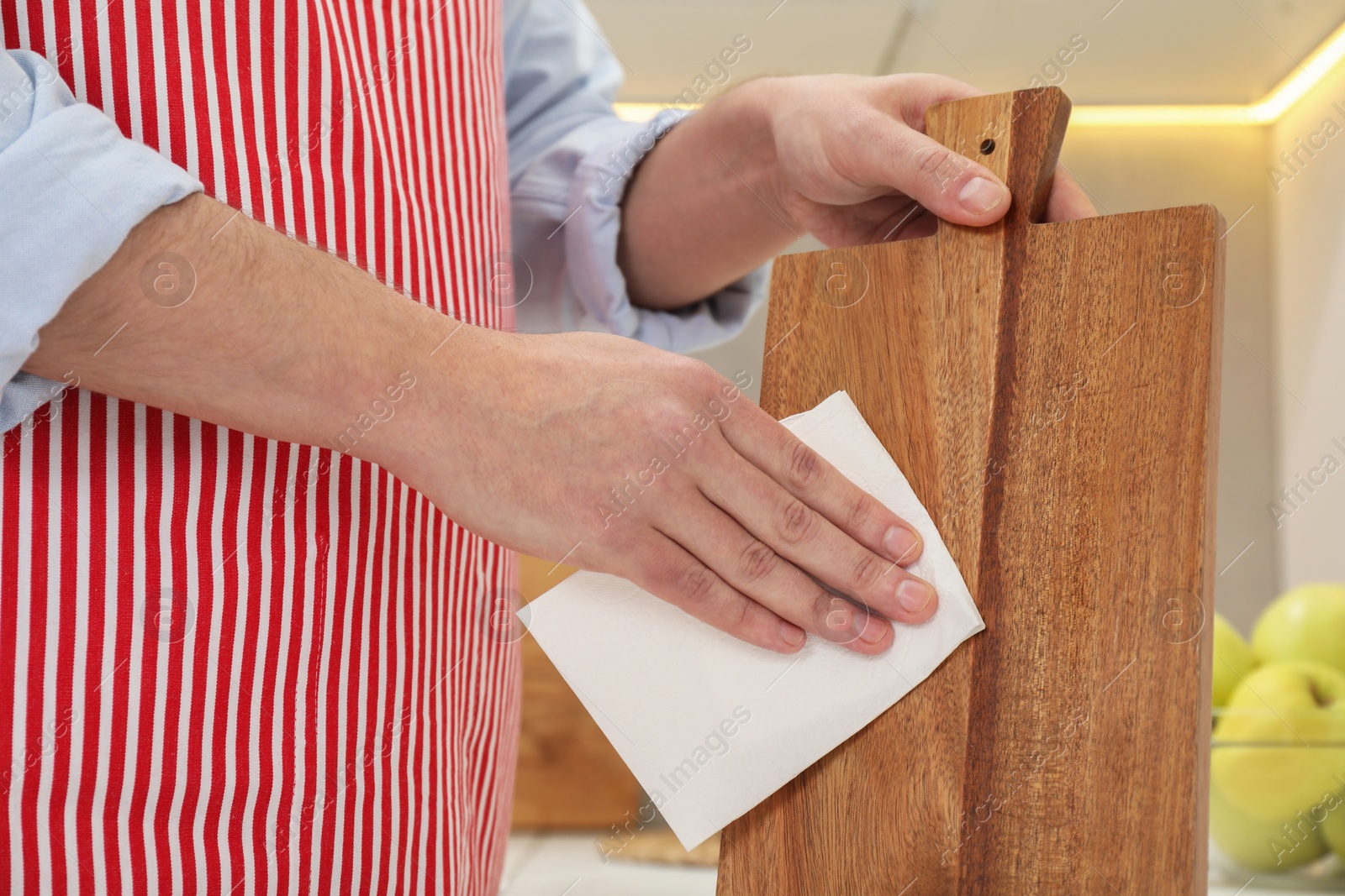 Photo of Man wiping wooden cutting board with paper napkin at home, closeup