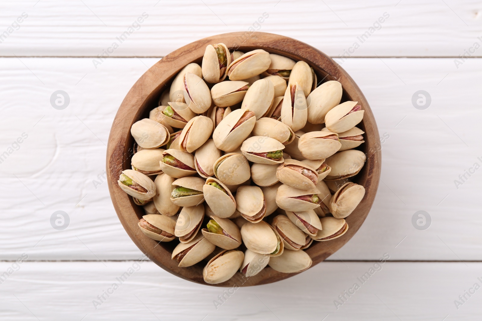 Photo of Tasty pistachios in bowl on white wooden table, top view