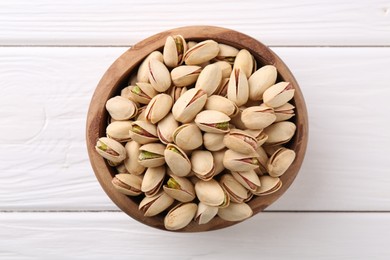 Photo of Tasty pistachios in bowl on white wooden table, top view