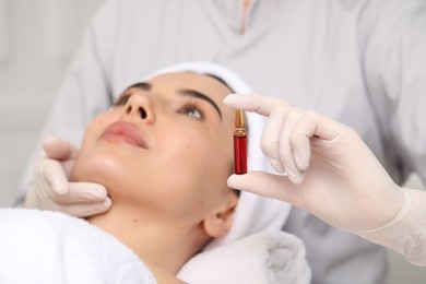 Photo of Professional cosmetologist holding skincare ampoule while working with client in clinic, closeup