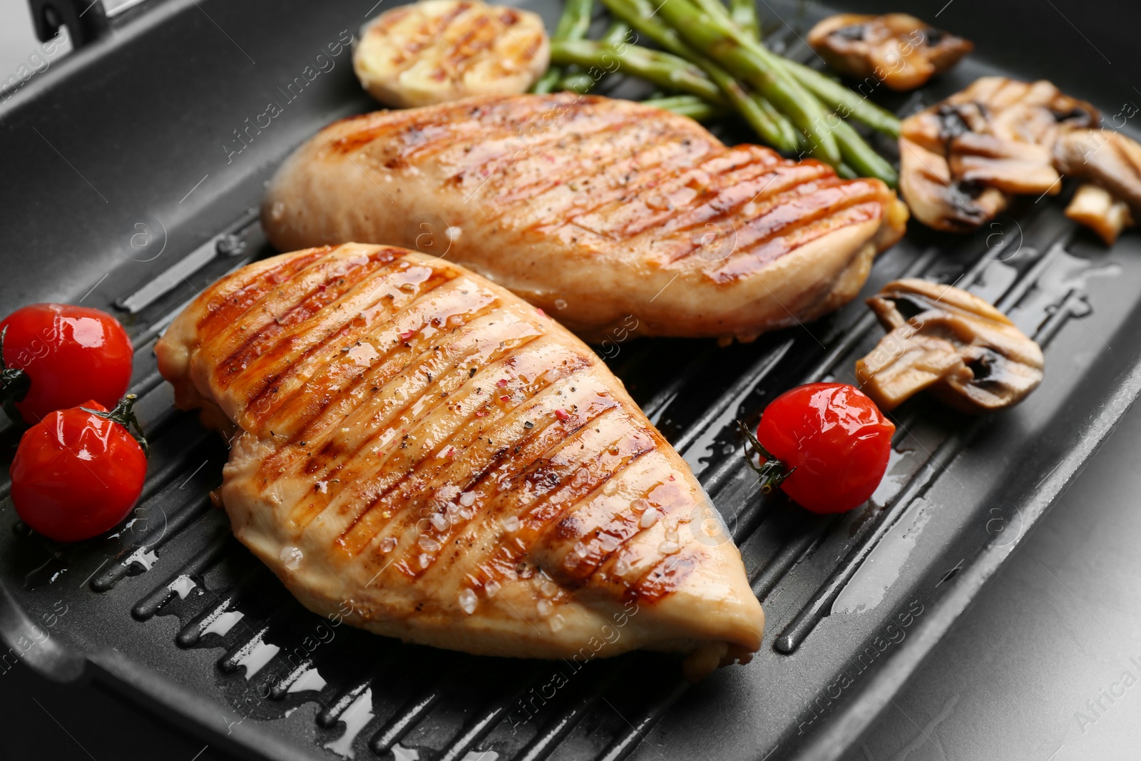 Photo of Tasty grilled chicken fillets and vegetables on frying pan, closeup