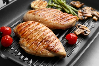 Photo of Tasty grilled chicken fillets and vegetables on frying pan, closeup