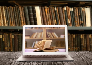 Online library. Modern laptop on wooden table and shelves with books indoors