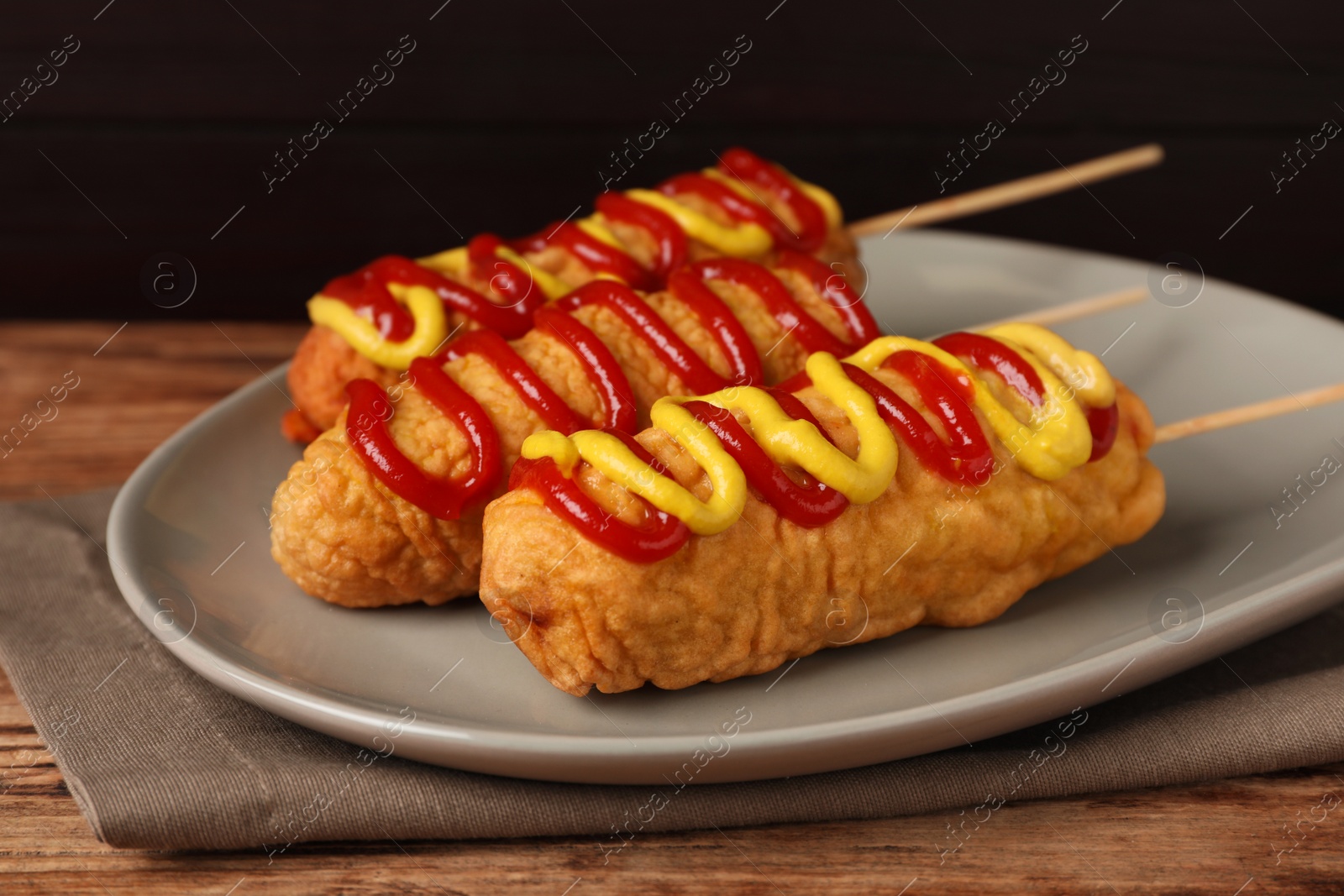 Photo of Delicious corn dogs with mustard and ketchup on wooden table, closeup