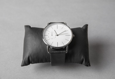 Small decorative pillow with stylish wrist watch on gray background. Fashion accessory