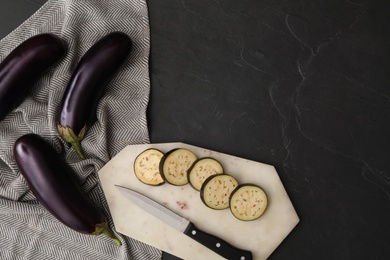 Photo of Cut and whole raw ripe eggplants on black table, flat lay. Space for text