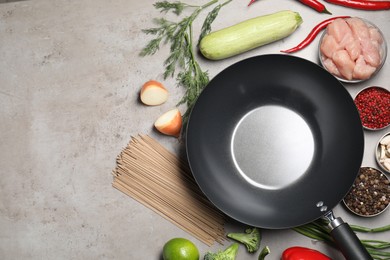 Photo of Empty iron wok surrounded by raw ingredients on grey table, flat lay. Space for text