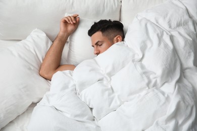 Photo of Handsome man sleeping under soft blanket in bed at home, above view