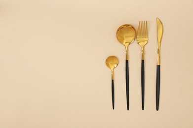 Photo of Stylish golden cutlery set on beige background, flat lay. Space for text