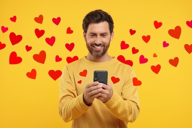 Long distance love. Man chatting with sweetheart via smartphone on golden background. Hearts flying out of device and swirling around him