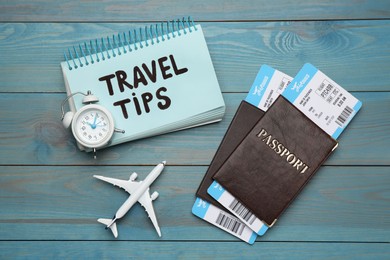 Photo of Notebook with phrase Travel Tips and tourist items on light blue wooden table, flat lay