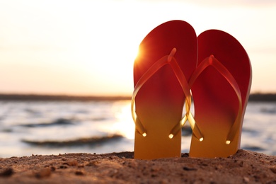 Photo of Stylish flip flops on sand near sea, space for text. Beach accessories