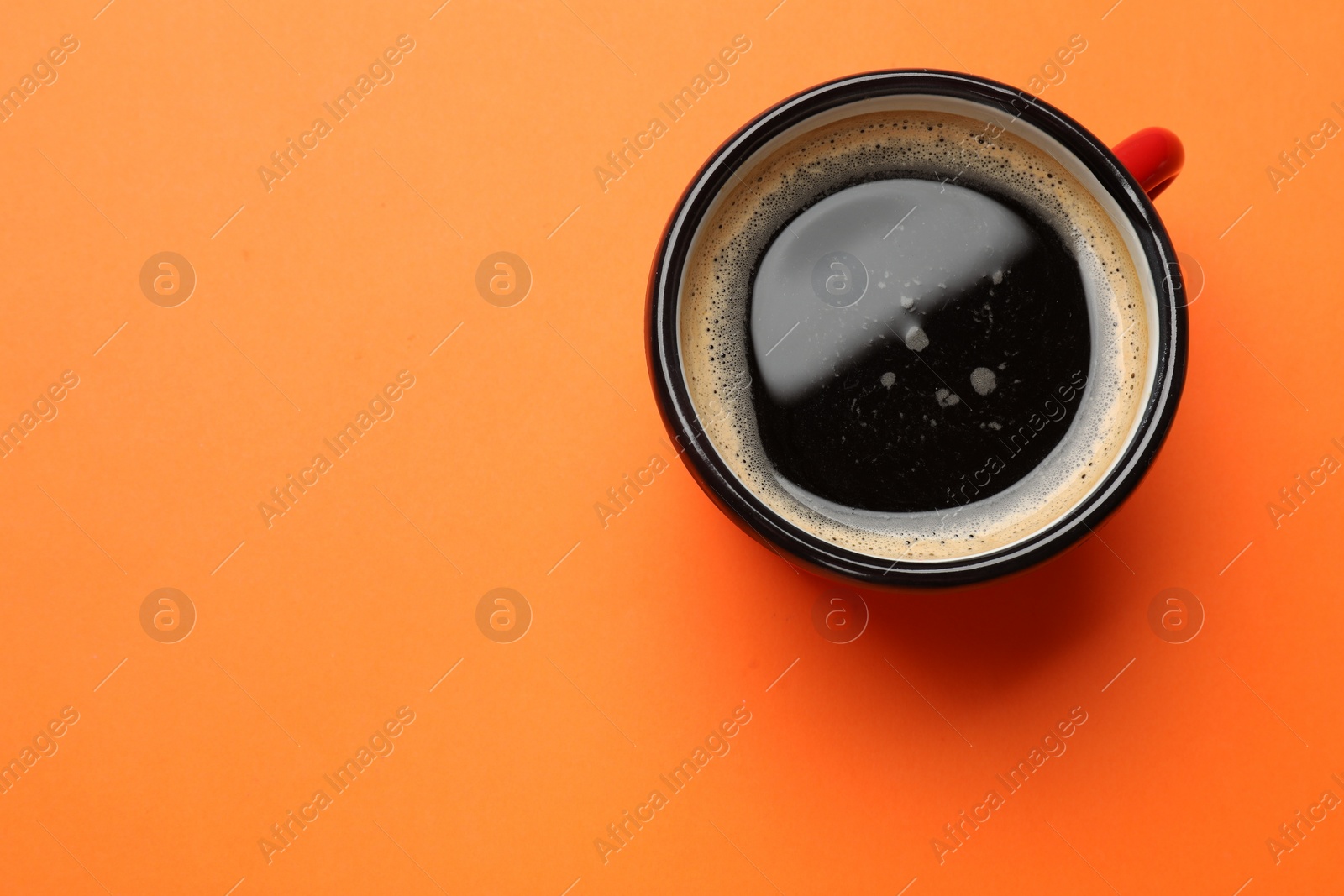 Photo of Fresh coffee in cup on orange background, top view. Space for text