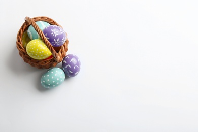 Wicker basket with painted Easter eggs on white background, top view